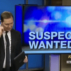 a man in a suit and tie talking on a cell phone in front of a screen that says suspect wanted