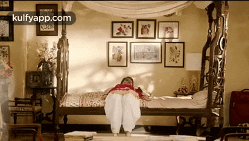 a woman is laying on a canopy bed in a room with pictures on the walls .