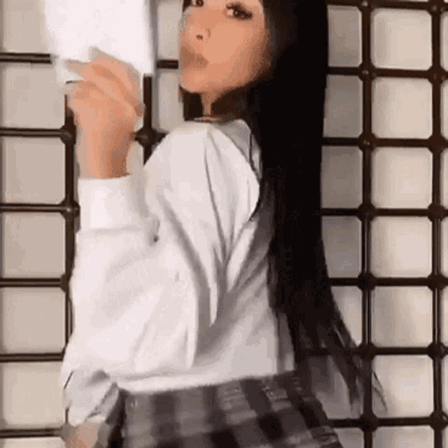 a woman in a white shirt and a plaid skirt is standing in front of a fence .