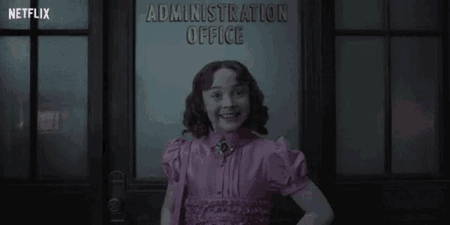 a little girl in a purple dress is standing in front of a door .