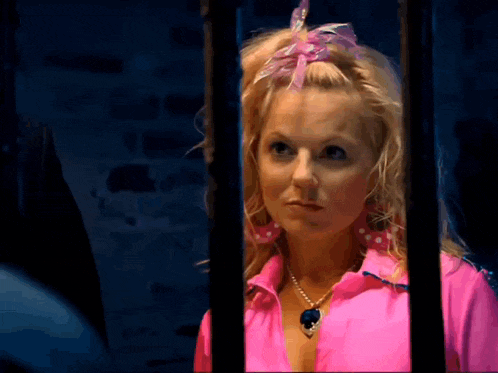 a woman wearing a pink shirt and a necklace behind bars