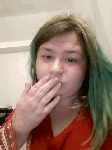 a woman with blue hair is covering her mouth with her hands