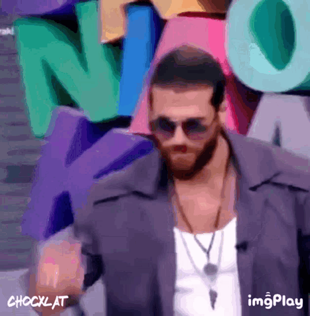 a man wearing sunglasses and a necklace stands in front of a sign that says noa