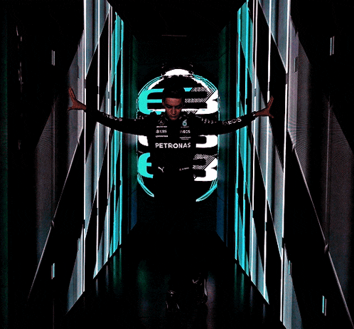 a man wearing a petronas shirt stands in a dark hallway