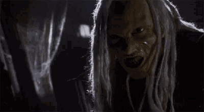a close up of a witch with dreadlocks and a scary face in a dark room .