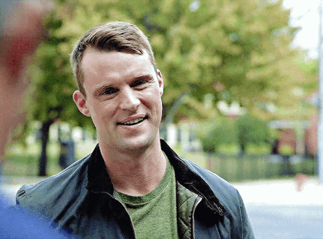 a man in a green shirt and a black jacket smiles
