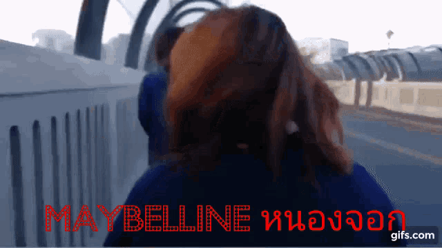 a woman stands in front of a sign that says " maybelline "