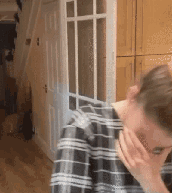 a woman in a plaid shirt covering her face with her hand