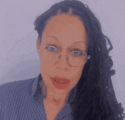 a woman wearing glasses and a blue striped shirt looks at the camera