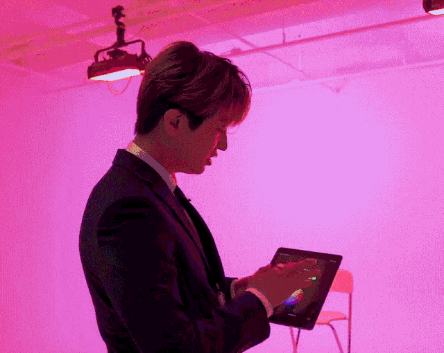 a man in a suit is using a tablet with a pink background
