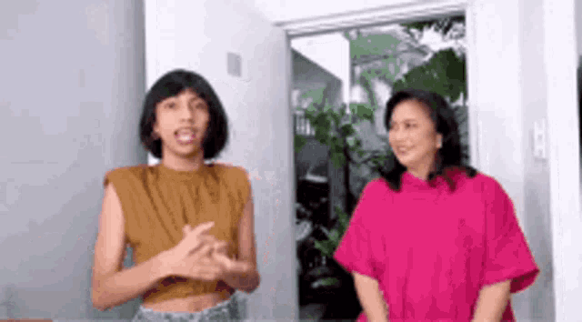 a woman in a pink shirt is standing next to a woman in a brown shirt .
