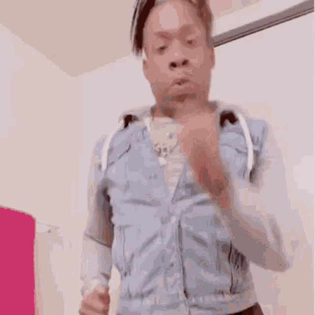 a man in a denim jacket is making a funny face while standing in a room .