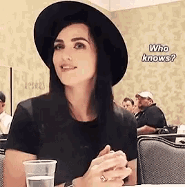 a woman wearing a hat and a ring is sitting at a table with a cup of water .