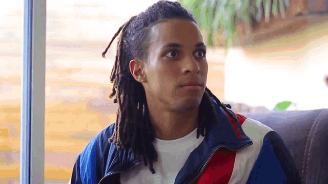 a young man with dreadlocks is wearing a jacket with a red white and blue stripe