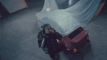 a man in a bandana is giving the middle finger next to a red car