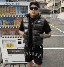 a man wearing sunglasses stands in front of a vending machine that says kizuna