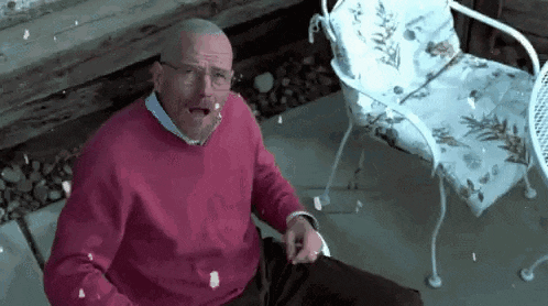a man in a pink sweater and glasses is sitting in a chair with a chair in the background .