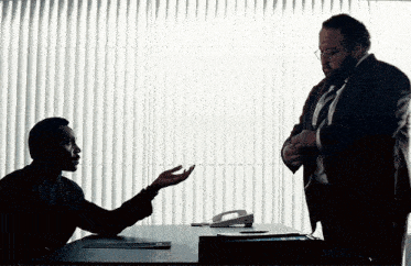 a man in a suit and tie is talking to another man in front of a window