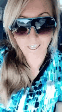 a woman wearing sunglasses and a blue shirt smiles at the camera