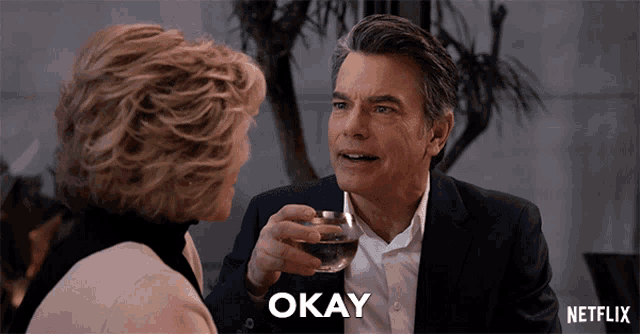 a man in a suit is holding a glass of wine and says okay
