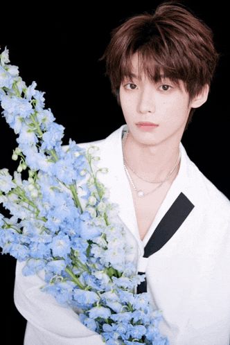 a young man in a white jacket is holding a bunch of blue flowers
