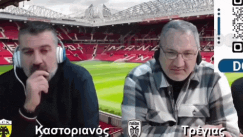 two men wearing headphones are sitting in front of a stadium that says man united on it
