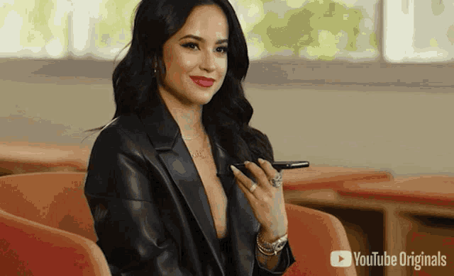 a woman in a black leather jacket is sitting in a chair holding a cell phone in her hand .
