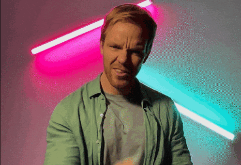a man in a green shirt is making a funny face in front of neon lights