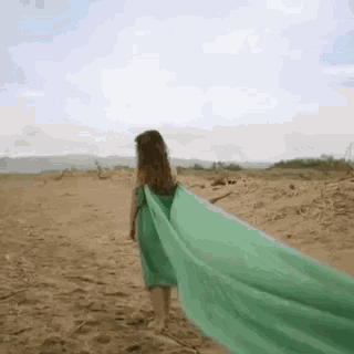 a woman in a green dress is walking across a sandy field .