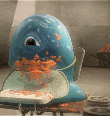 a blue monster is eating a piece of bread on a school desk