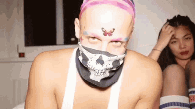 a man wearing a bandana with a skull on it looks at the camera while a woman sits behind him .