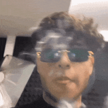 a man wearing sunglasses is smoking a cigarette in a car