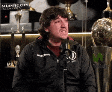 a man wearing a marathon jacket is speaking into a microphone