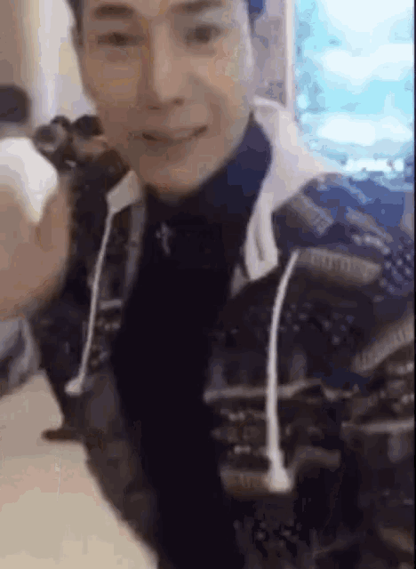 a man in a black turtleneck and a hoodie is smiling and holding a white object .