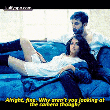 a man and a woman are laying on a blue couch and the woman is laying on the man 's lap