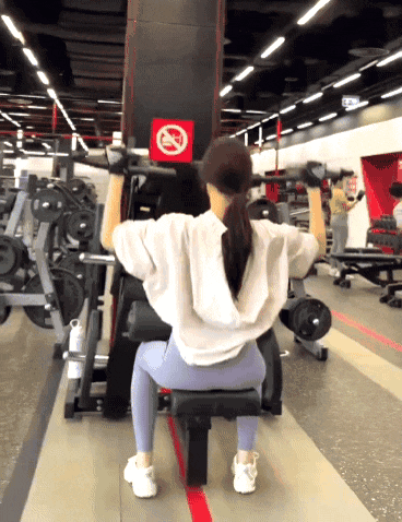 a woman is lifting dumbbells in a gym with a no smoking sign in the background