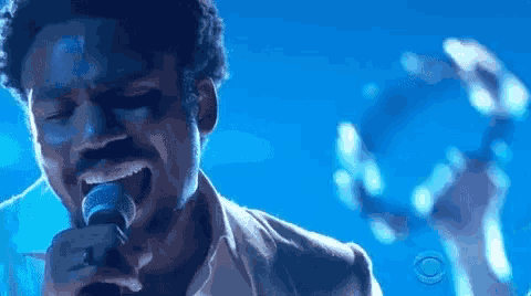 a man is singing into a microphone with a tambourine in the background