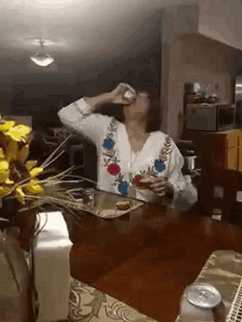 a woman is drinking from a glass while sitting at a table .