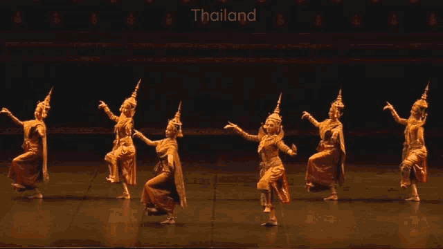 a group of people are dancing in front of a sign that says thailand on it