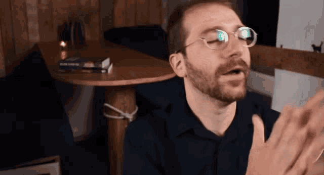 a man wearing glasses is clapping his hands in front of a table