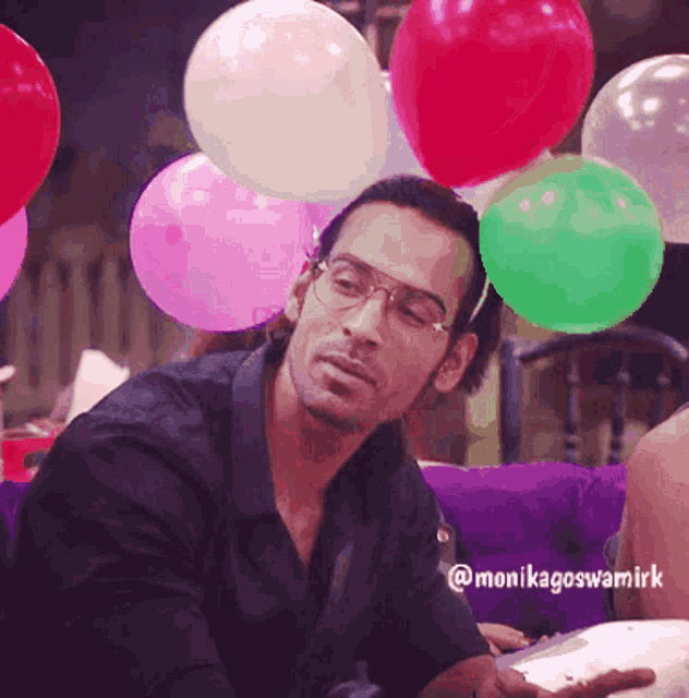 a man wearing glasses is sitting in front of balloons with the hashtag monikagoswamiirk