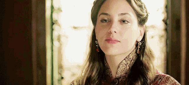 a woman wearing earrings and a braided headband looks at the camera