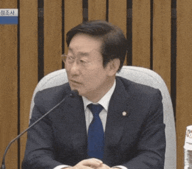 a man in a suit and tie is sitting in front of a microphone with a sign that says 청조사 on it