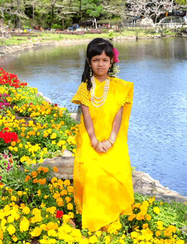 a little girl in a yellow dress is standing in front of a pond