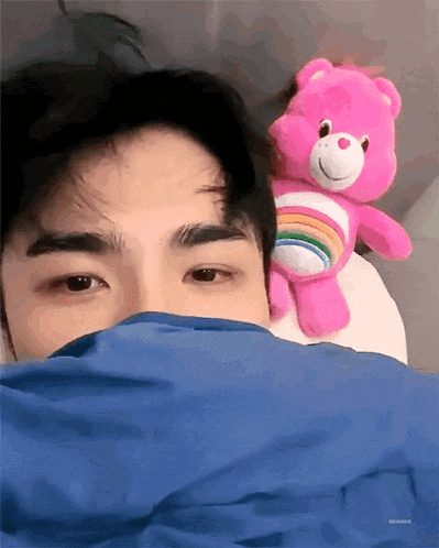 a man is laying in bed with a pink care bear on his head