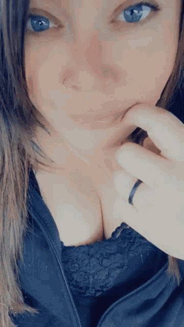 a close up of a woman 's face with blue eyes and a black ring on her finger .