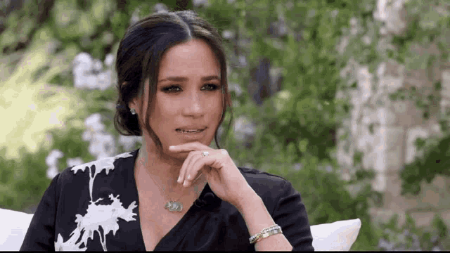 a woman is sitting on a couch with her hand on her chin and a necklace on her neck .