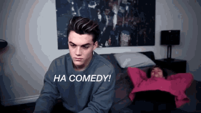 a man sitting next to a woman laying on a bed with the words ha comedy written on the bottom