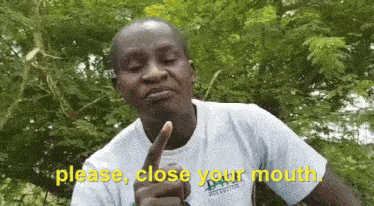 a man in a white shirt is making a funny face while pointing at his mouth .