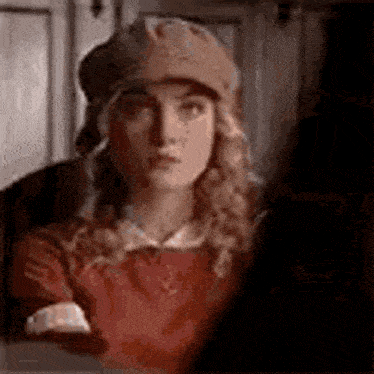 a woman wearing a hat and a red shirt is looking at the camera .